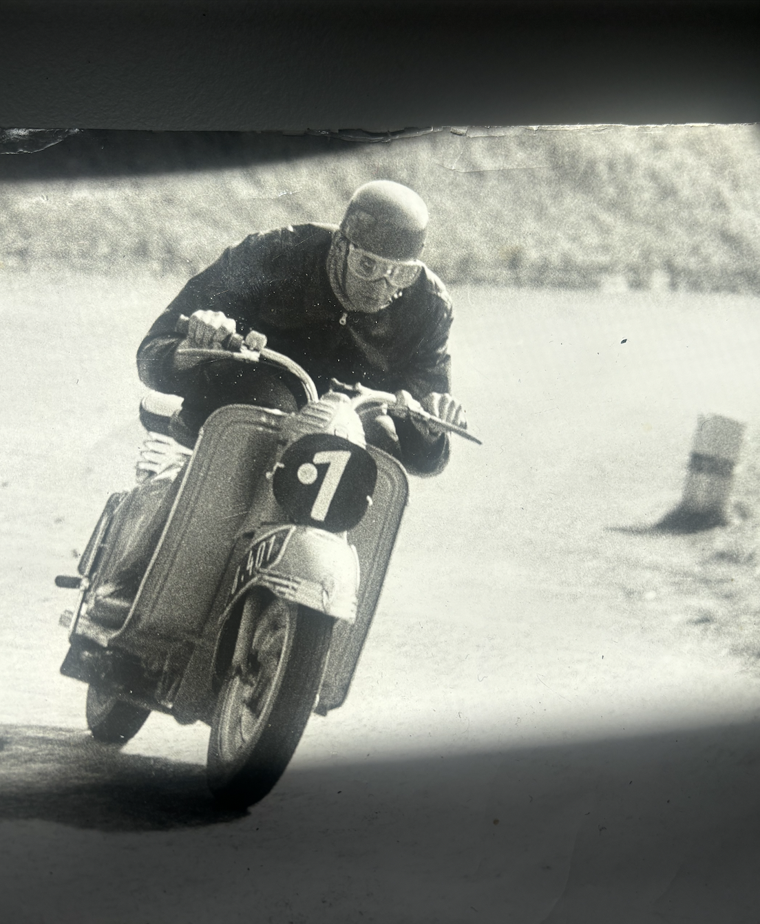 Schwarz-weiß-Pressefoto eines Motorradfahrers in Rennmontur, in einer Kurve beim historischen Gaisbergrennen 1955.
